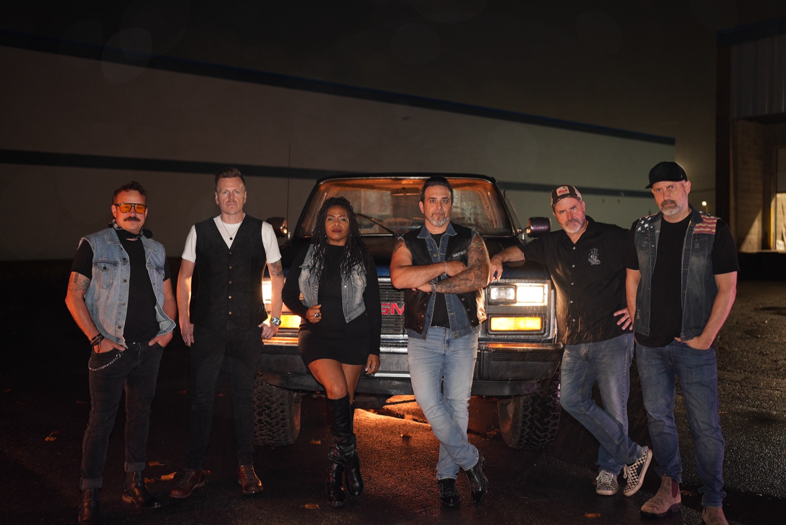 The six members of Lights Above the Mesa standing in front of a pickup truck at night, headlights on.