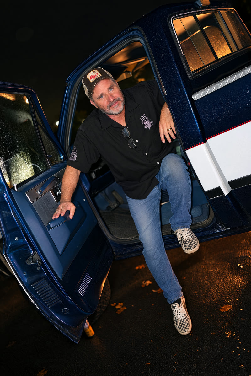 Keith (guitar) in a trucker cap, stepping out of the truck's open door.